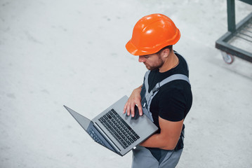 Aerial view. With laptop in hands. Industrial worker indoors in factory. Young technician with...