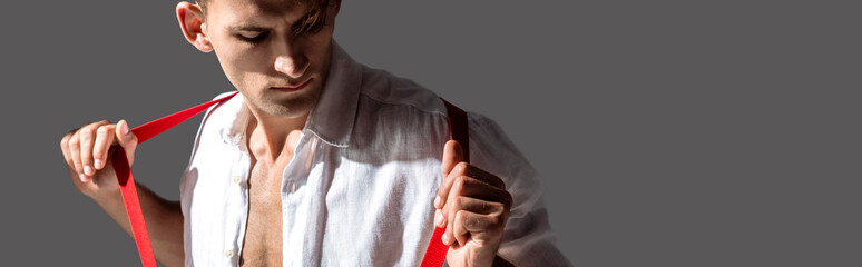 panoramic shot of man in shirt touching red suspenders isolated on grey