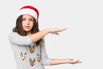 Little girl celebrating christmas day shocked and amazed holding a copy space between hands.
