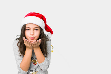 Little girl celebrating christmas day folding lips and holding palms to send air kiss.