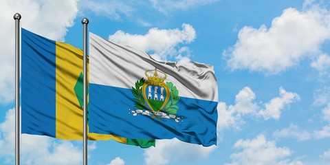 Saint Vincent And The Grenadines and San Marino flag waving in the wind against white cloudy blue...