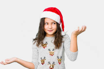 Little girl celebrating christmas day doubting and shrugging shoulders in questioning gesture.