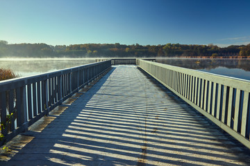 Obraz premium frosted wooden bridge and fog on the lake early in the morning in Poland.