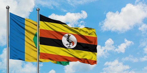 Saint Vincent And The Grenadines and Uganda flag waving in the wind against white cloudy blue sky...