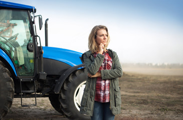 Pensive woman near the tractor on the background of the field.