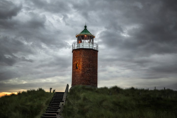 Fototapeta na wymiar Brickstone lighthouse on high grass hills on Sylt at North Sea