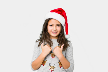 Little girl celebrating christmas day raising both thumbs up, smiling and confident.