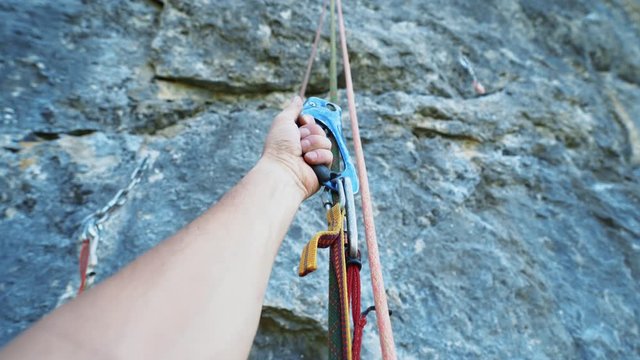 climbing gear closeup POV. First person view of male hand with ascender device attached to rope, several ropes on which a person hangs.