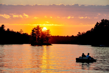 sunset on a Muskoka, Ontario lake with two women in silhouette in their paddleboat,