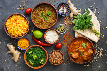 Assorted various Indian food on a dark rustic background. Traditional Indian dishes - Chicken tikka masala, palak paneer, saffron rice, lentil soup, pita bread and spices. Top view, flat lay.