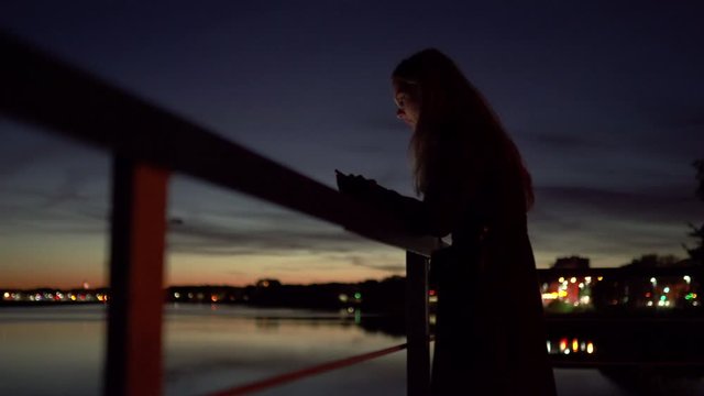 Sad young woman standing on a pier - Vivid night on a river with bokeh light in the background - 1.4 aperture thin dop