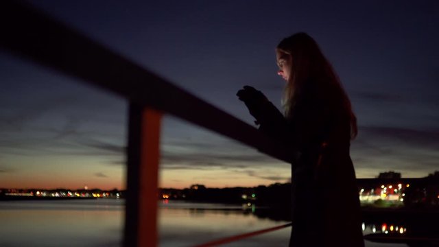 Sad young woman standing on a pier - Vivid night on a river with bokeh light in the background - 1.4 aperture thin dop