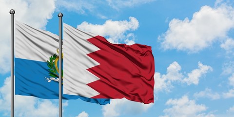 San Marino and Bahrain flag waving in the wind against white cloudy blue sky together. Diplomacy...
