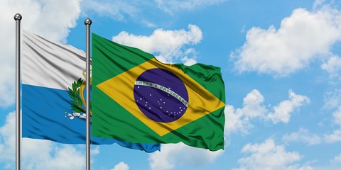 San Marino and Brazil flag waving in the wind against white cloudy blue sky together. Diplomacy concept, international relations.