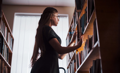 Standing on the ladder. Female student is in library that full of books. Conception of education