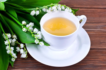 Cup of green tea with lily of the valley or may bells flowers on a wooden background.