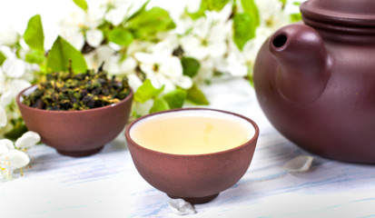 Green tea and dried leaves of tieguanyin tea in a ceramic cups with branches of blossoming apple tree on a white wooden background.