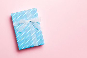 Gift box with white bow in hands for Christmas or New Year day on pink background, top view with copy space