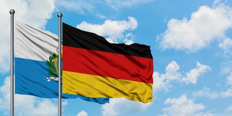 San Marino and Germany flag waving in the wind against white cloudy blue sky together. Diplomacy...
