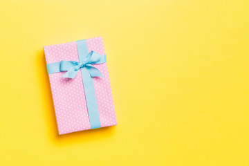 Gift box with blue bow for Christmas or New Year day on yellow background, top view with copy space