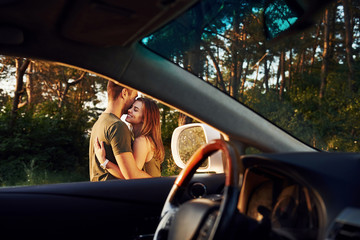 View from the car's interior. Steering wheel, side mirror. Beautiful young couple have a good time in the forest at daytime