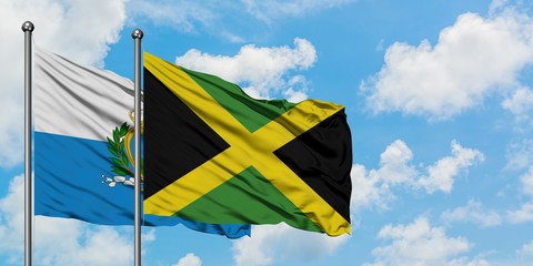 San Marino and Jamaica flag waving in the wind against white cloudy blue sky together. Diplomacy concept, international relations.