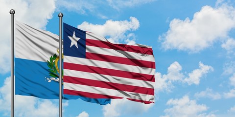Obraz premium San Marino and Liberia flag waving in the wind against white cloudy blue sky together. Diplomacy concept, international relations.