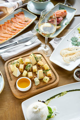 Cheese plate. Focus on delicious cheese mix with walnuts, honey on wooden table. Various snacks and antipasti on the table. Restaurant menu.