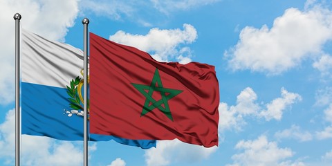 San Marino and Morocco flag waving in the wind against white cloudy blue sky together. Diplomacy...