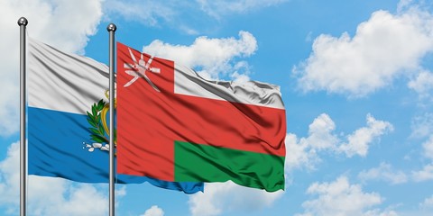 San Marino and Oman flag waving in the wind against white cloudy blue sky together. Diplomacy...