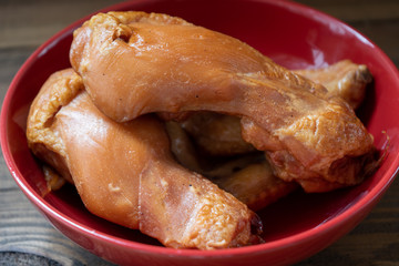Fresh smoked chicken legs in a red plate on a brown wooden background. Close-up