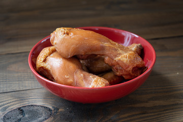 Fresh smoked chicken legs in a red plate on a brown wooden background. 