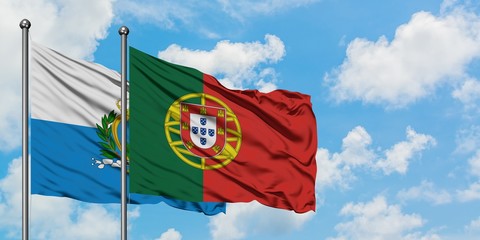 San Marino and Portugal flag waving in the wind against white cloudy blue sky together. Diplomacy...