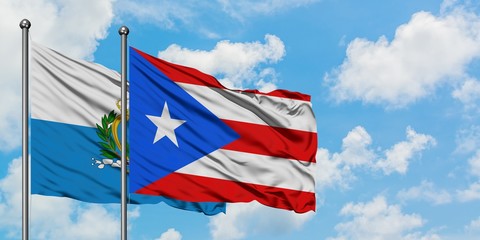 San Marino and Puerto Rico flag waving in the wind against white cloudy blue sky together....