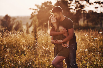 In the field illuminated by the sunlight. Beautiful young couple have a good time in the forest at daytime