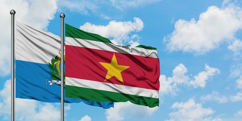San Marino and Suriname flag waving in the wind against white cloudy blue sky together. Diplomacy concept, international relations.