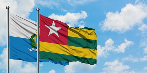 San Marino and Togo flag waving in the wind against white cloudy blue sky together. Diplomacy concept, international relations.