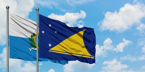 San Marino and Tokelau flag waving in the wind against white cloudy blue sky together. Diplomacy...