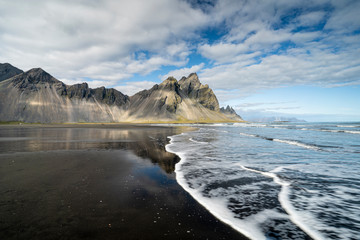vestrahorn in southern Iceland, mirroring in calm water over black volcanic beach, landscape 