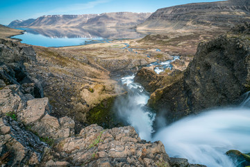 On top of a waterfall called Dynjandi in the Westfjords of Iceland. Mountains and blue sky reflects in the calm ocean. Nature and landscape concept.