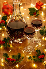 A decanter of port and crystal glasses with christmas lights, baubles holly berryies and christmas decorations