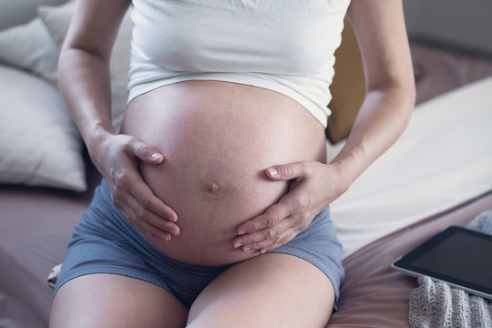 A pregnant woman lovingly touches her belly in her bedroom