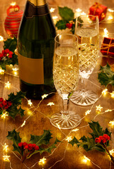 Champagne flutes and bottle with christmas lights, baubles, holly berries and christmas decorations