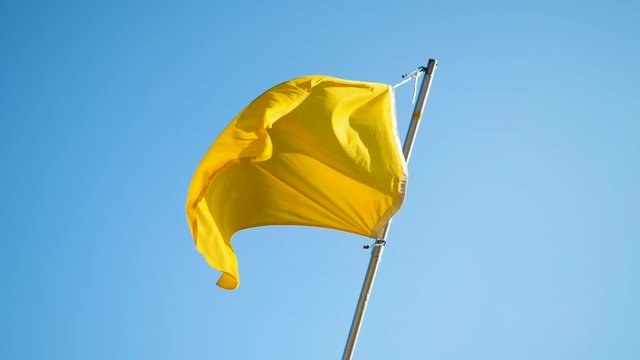 Yellow flag waving in the wind on the beach against blue sky. Slow motion. HD