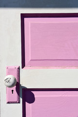 A vintage farmhouse pink and white painted door with strong shadows in bright sunlight.