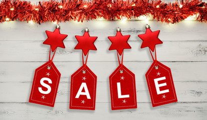 A string of christmas star decorations, lights and tinsel, with for sale written on red labels, on destressed white wood