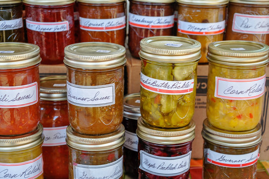 Macro of jars of homemade pickles, jams and preserves are neatly displayed and await buyers at a farmer's market.