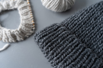 Knitting at home during the day from natural yarn from wool and alpaca in natural color with bamboo knitting needles and knitted hat on the grey background. Handwork, hobby. Close-up