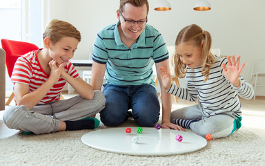 Happy young father plays with his two cheerful siblings children Board Game with colorful dices
