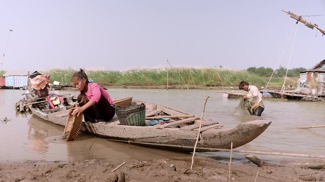 Clammer pouring clams into a bamboo basket held by his wife sitting in a dugout canoe